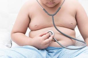 Obese fat boy check stomach by stethoscope. photo