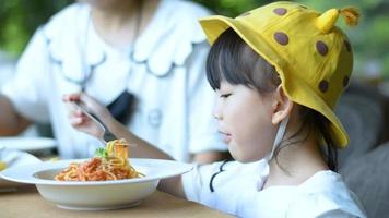 Close up portrait of a Little Asian girl with yellow hat eats spaghetti . video