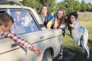 Young cheerful girls are pushing an old car. Women in the style of the 90s. photo