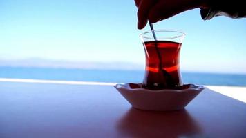 Trinken ein Tasse von Tee im das Blau Meer Aussicht auf ein sonnig Tag, Mischen Tee Zucker und Trinken Tee, selektiv Fokus video