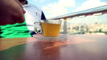 camarero trae un taza de herbario té, joven hombre es Bebiendo un taza de herbario té en café en un soleado día, selectivo atención video