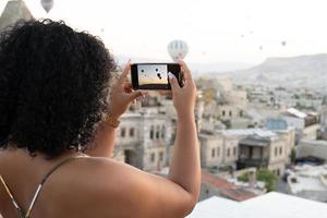 a tourist takes photos of hot air balloons in the mountains of Cappadocia on a mobile phone.