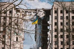 Flag of Ukraine against the background of a destroyed building in Ukraine. The building was destroyed by a Russian air bomb photo
