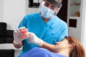 hermosa mujer recepción explicaciones acerca de su dental tratamiento con su dentista. médico utilizando un dental modelo. foto