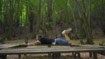 Jeune aventurier travail avec portable dans la nature. Jeune homme est travail avec portable mensonge vers le bas sur une séance banc. video