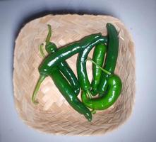 Ripe green chilies in a bamboo basket on a green background. photo