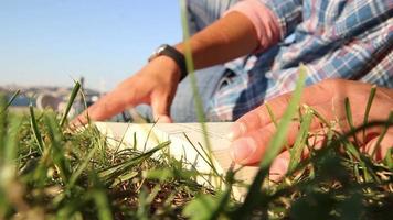 uomo lettura un' libro dire bugie su erba nel un' città parco, uomo lettura libro e girare pagine nel città parco con un' mare Visualizza, selettivo messa a fuoco video