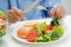 Asian elderly woman patient eating salmon stake and vegetable salad for healthy food in hospital. photo