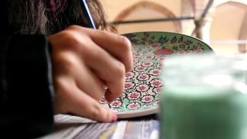 artista donna vernici storico motivi, utilizzando spazzola e dipingere per rendere ottomano piastrella porcellana motivo arte, selettivo messa a fuoco video