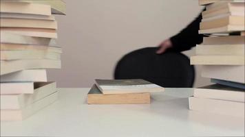 Student sitting at desk to read a book among piles of books, student opening the page of the reading book at the desk and reading the book, selective focus video