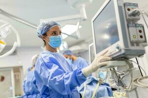 Anesthesiologist keeping track of vital functions of the body during cardiac surgery. Surgeon looking at medical monitor during surgery. Doctor checking monitor for patient health status. photo