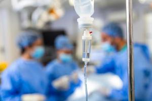 Close-up of IV drip bag in emergency room. Medicine is passing through pipe from intravenous drip. It is in hospital. Surgery in background photo