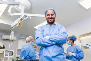 Portrait of male surgeon in operation theater looking at camera. Doctor in scrubs and medical mask in modern hospital operating room. photo