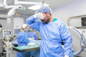 tenso cirujano con manos en cara en operando habitación en hospital. agotado cirujano después largo cirugía foto