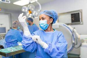 Portrait of beautiful female doctor surgeon putting on medical gloves standing in operation room. Surgeon at modern operating room photo