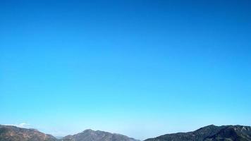 azul cielo con blanco nubes y montañas abajo, antecedentes con blanco impresión antecedentes foto