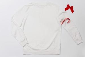 Close up white blank template sweatshirt with copy space and Christmas Holiday concept. Top view mockup hoodie and red holidays decorations on white background. Happy New Year accessories. Xmas outfit photo