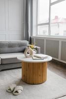 Wooden coffee table with marble top in the interior of a modern living room with a gray sofa photo