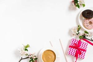 Stylish flat lay with a cup of coffee, apple blossoms, donuts and a gift box of birthday or valentine's sweets on a white background with copy space photo