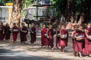 BAGAN, MYANMAR - JUL 18, 2018-Buddhist novices walk to collect alms and offerings along the road at Bagan, Myanmar. photo