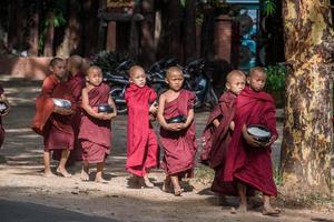 BAGAN, MYANMAR - JUL 18, 2018-Buddhist novices walk to collect alms and offerings along the road at Bagan, Myanmar. photo