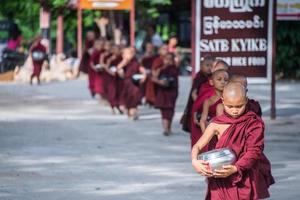 BAGAN, MYANMAR - JUL 18, 2018-Buddhist novices walk to collect alms and offerings along the road at Bagan, Myanmar. photo