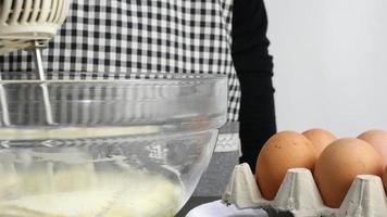 cocinero es haciendo crema pastel utilizando eléctrico portátil mezclador máquina, hogar panadería Cocinando concepto video