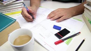 Student studying with test book in piles of books and drinking coffee, Student solves test questions to prepare for exam, selective focus video