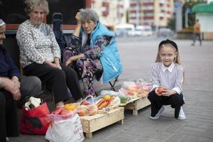 un pequeño niña sostiene vegetales a el será de antiguo calle vendedores. foto