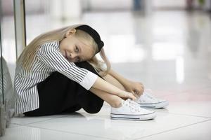 un cansado niño en un urbano ajuste. un niña de elemental años se sienta en el piso de un tienda. foto