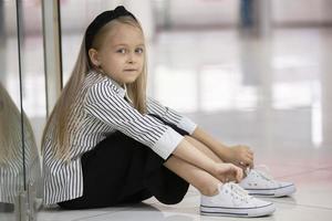 un hermosa niña se sienta en el piso de el almacenar. un niño de elemental edad. foto