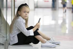 hermosa pequeño niña en un urbano ajuste con un teléfono. foto