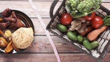 comida chatarra, verduras frescas y cinta métrica en la mesa de madera video