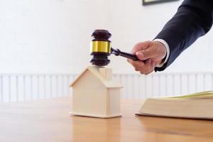 A real estate auctioneer holds a gavel in his hand to knock on a real estate auction when the final price is reached. Real estate auction concept with gavel knocking on mockup house photo