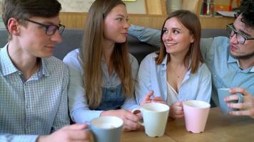 Young friends sit in a cafe, drink coffee and have fun communicating. Slow motion video