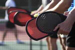 Photo of a pickle ball and racquet on a pickle ball court..