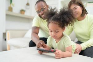 pequeño niños jugar y aprender cosas en el amplio mundo en tableta. con padres a supervisar y ayuda en el vivo habitación de el casa en vacaciones foto