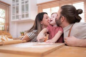 Mom and dad in the kitchen of the house with their small children. Have a good time baking bread and making dinner together. photo