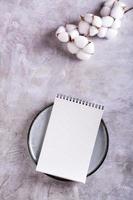 Mockup of an open notebook on a plate and a branch of cotton on a gray background top and vertical view photo