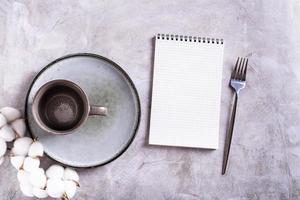 Empty ceramic mug, plate, cotton and blank open notebook on gray background top view photo