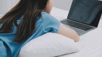 efficiente giovane del Millennio ragazza seduta su un' letto nel il mattina, usi il computer portatile computer e mangia Cornetti e bevande caffè per prima colazione. superiore giù sparo. video