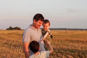 papá con dos hijos en el campo a puesta de sol. concepto de simpático familia y de verano vacaciones foto