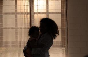 madre y niños disfrutar el Mañana luz de sol brillante mediante el dormitorio ventana en el casa. foto