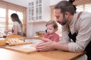 Mom and dad in the kitchen of the house with their small children. Have a good time baking bread and making dinner together. photo