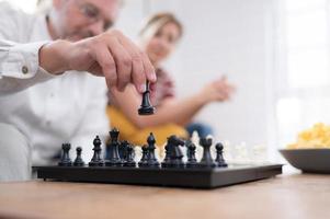 In the living room of the house, an elderly couple sits and relaxes. to begin playing chess together with a chess board with a daughter cheering beside him photo