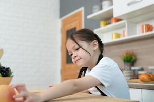 retrato de un pequeño niña en el cocina de un casa teniendo divertido jugando con Fruta juguete y batería de cocina foto