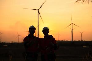 Engineers working on wind farms for renewable energy are responsible for maintaining large wind turbines. Returning from work during while the evening sun shines a beautiful golden light upon both of photo