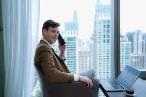 Young businessman sit and relax in the relaxation room by the window overlooking the beautiful city buildings. along with the phone to talk about business. photo