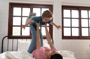 Little boy flying with mom using her legs to help him fly high off the floor of his bed in the bedroom. photo