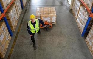 Worker in auto parts warehouse use a handcart to work to bring the box of auto parts into the storage shelf of the warehouse waiting for delivery to the car assembly line photo